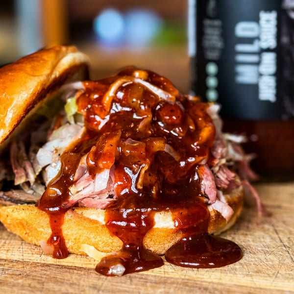 Juicy pulled pork sandwich with BBQ sauce on a brioche bun, next to a sauce bottle.