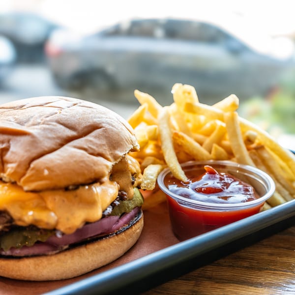 Cheeseburger with melted cheese, pickles, and red onion, served with fries and ketchup on a tray.
